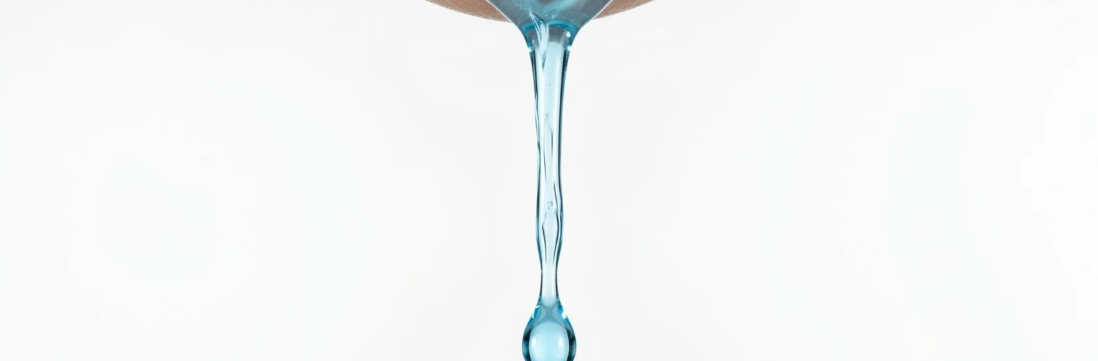 Sérum azul escorrendo em fio contínuo até formar uma gota, macro em fundo claro